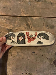 Vassoio allungato in gres con quattro ritratti femminili e dettagli rossi, lunghezza circa 35 cm; larghezza circa 8 cm